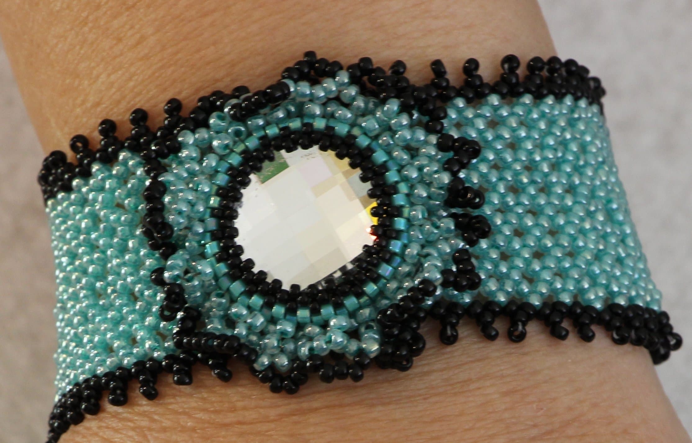1095. Hand woven beaded bracelet with a 20mm crystal bezeled in turquoise and black beads. Slide bar clasp
